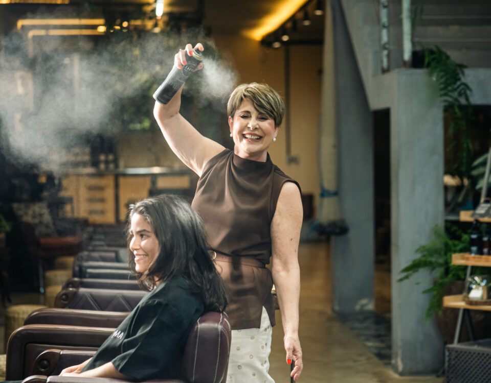 Imagem ilustrativa da Valéria finalizando um penteado e sorrindo para a foto.